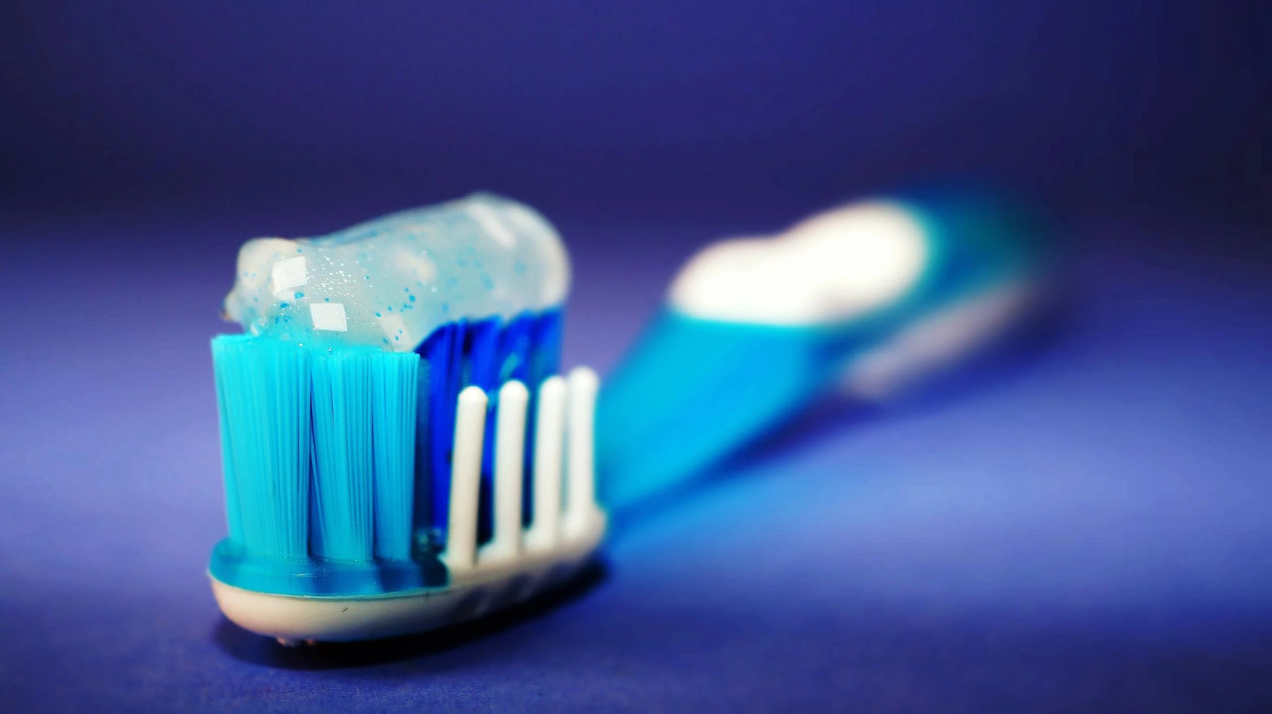 blue sparkly tooth paste on a blue toothbrush with purple background